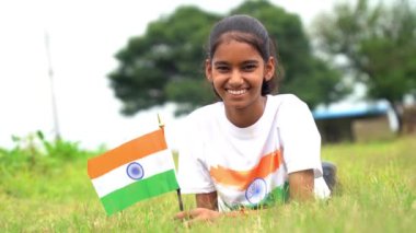 Elinde Kızılderili bayrağı tutan ve gülümseyen sevimli bir Hintli kız. Hindistan 'da Bağımsızlık Günü veya Cumhuriyet Günü' nü kutluyoruz. Tiranga 'nın gururunu gösteren bir kız. Har Ghar Tiranga