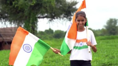 Elinde Kızılderili bayrağı tutan ve gülümseyen sevimli bir Hintli kız. Hindistan 'da Bağımsızlık Günü veya Cumhuriyet Günü' nü kutluyoruz. Tiranga 'nın gururunu gösteren bir kız. Har Ghar Tiranga