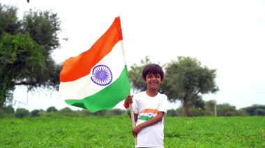 Mutlu Hindistan Sevimli Gülümseyen küçük çocuk dışarıda parka üç renkli bayrak sallayarak Bağımsızlık Günü 'nü veya Cumhuriyet Günü' nü kutluyor..