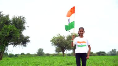 Elinde Kızılderili bayrağı tutan ve gülümseyen sevimli bir Hintli kız. Hindistan 'da Bağımsızlık Günü veya Cumhuriyet Günü' nü kutluyoruz. Tiranga 'nın gururunu gösteren bir kız. Har Ghar Tiranga