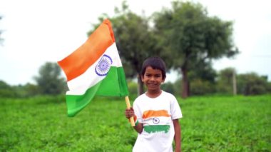 Mutlu Hindistan Sevimli Gülümseyen küçük çocuk dışarıda parka üç renkli bayrak sallayarak Bağımsızlık Günü 'nü veya Cumhuriyet Günü' nü kutluyor..
