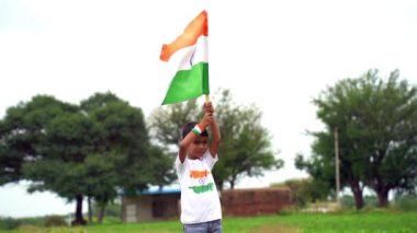 Mutlu Hindistan Sevimli Gülümseyen küçük çocuk dışarıda parka üç renkli bayrak sallayarak Bağımsızlık Günü 'nü veya Cumhuriyet Günü' nü kutluyor..