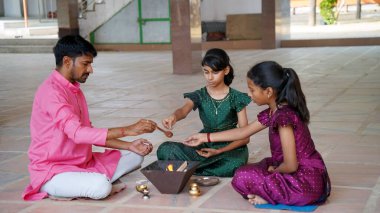 Geleneksel kıyafetli bir Hintli aile, evlerinde enerjilerini dengelemek için bir rahip tarafından yönetilen Yagya veya Havan 'ı icra eder. Bu kutsal pooja uyum ve pozitif enerji içindir..