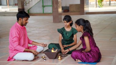 An Indian family in traditional attire performs a Yagya or Havan, led by a priest, to balance energies in their home. This sacred pooja is for harmony and positive energy. clipart