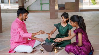 Geleneksel kıyafetli bir Hintli aile, evlerinde enerjilerini dengelemek için bir rahip tarafından yönetilen Yagya veya Havan 'ı icra eder. Bu kutsal pooja uyum ve pozitif enerji içindir..