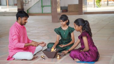 An Indian family in traditional attire performs a Yagya or Havan, led by a priest, to balance energies in their home. This sacred pooja is for harmony and positive energy. clipart