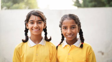 Mutlu Hintli okul çocuğu portresi ya da üniformalı çocuklar sınıfta kitap ve dizüstü bilgisayarla çalışırken el kaldırıyorlar. Çevrimiçi ders öğreniliyor.