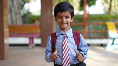 Sırt çantalı, kameraya bakan gülümseyen Hintli kırsal okul çocuğu. Gülümseyen bir okul üniforması giyen neşeli bir çocuk. İlkokul ve ilköğretim.
