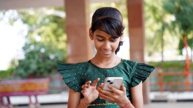 Genç ve mutlu bir Hintli kız akıllı telefonuyla e-postaları ve sohbetleri kontrol ediyor, haberleri ve güncellemeleri kolaylıkla okuyor. Evde rahat, o zahmetsizce bağlı kalmaktan hoşlanıyor.