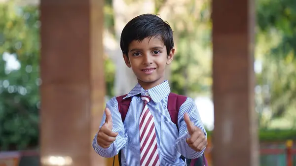 Sırt çantalı, kameraya bakan gülümseyen Hintli kırsal okul çocuğu. Gülümseyen bir okul üniforması giyen neşeli bir çocuk. İlkokul ve ilköğretim.