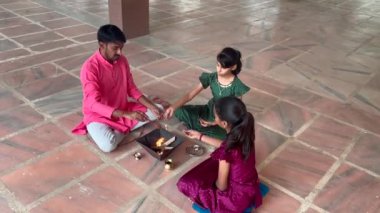 Geleneksel kıyafetli bir Hintli aile, evlerinde enerjilerini dengelemek için bir rahip tarafından yönetilen Yagya veya Havan 'ı icra eder. Bu kutsal pooja uyum ve pozitif enerji içindir..
