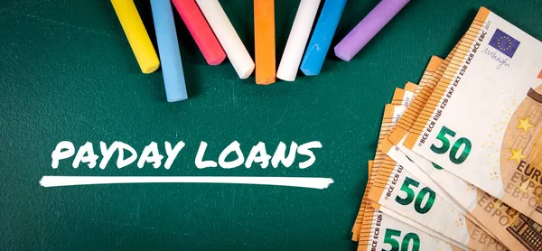 PAYDAY LOANS. Money and colored pieces of chalk on a green board.