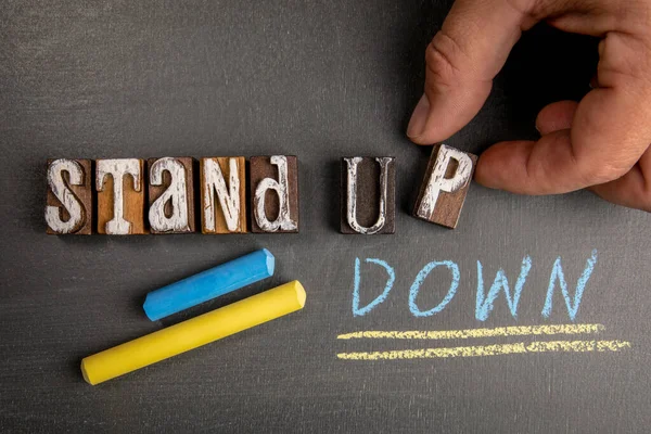 stock image Stand Up and Stand Down. Wooden letter blocks on a dark chalkboard background.