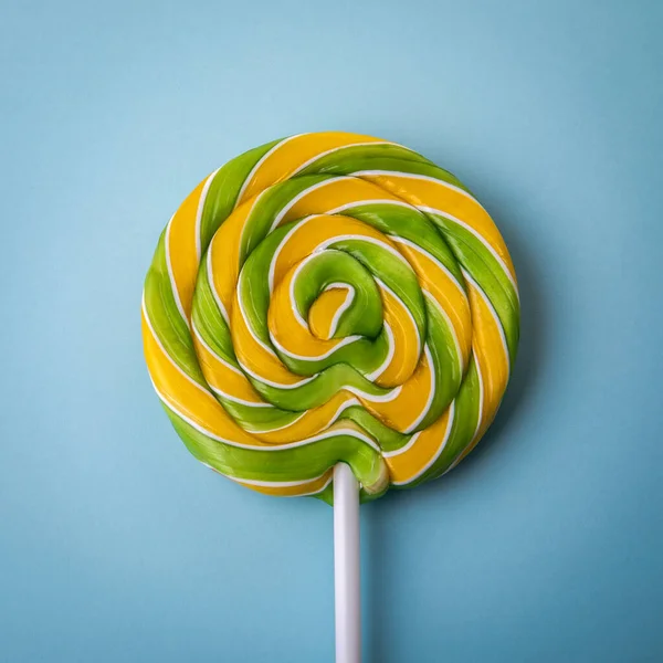 Colorful green-yellow candy, lollipop on a stick on a blue background.
