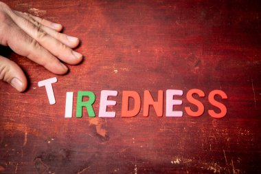 TIREDNESS Concept. Text from colorful letters on wood texture background.