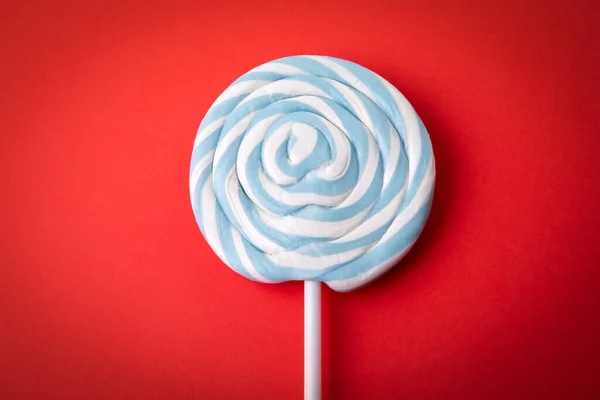 Blue candy on a stick, lollipop. Red background.