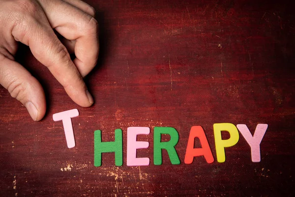 THERAPY concept. Text from colored letters on a painted wooden background.