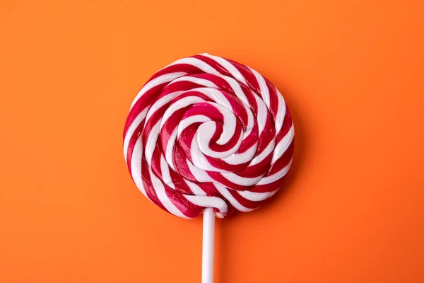 Red and white candy on a stick, lollipop. Orange background.