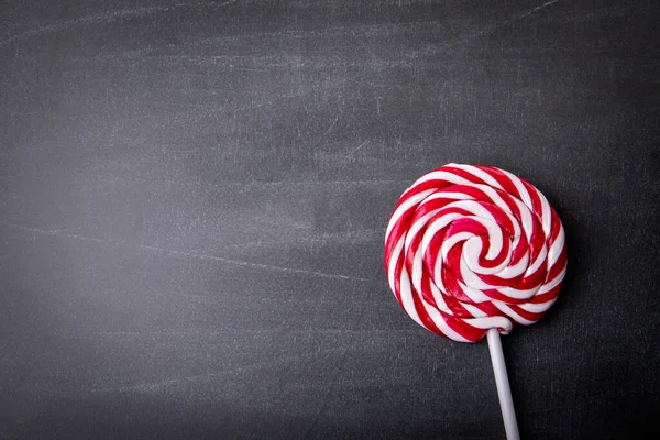Red candy on a stick, lollipop. Dark chalkboard background. Copy space, mock up.
