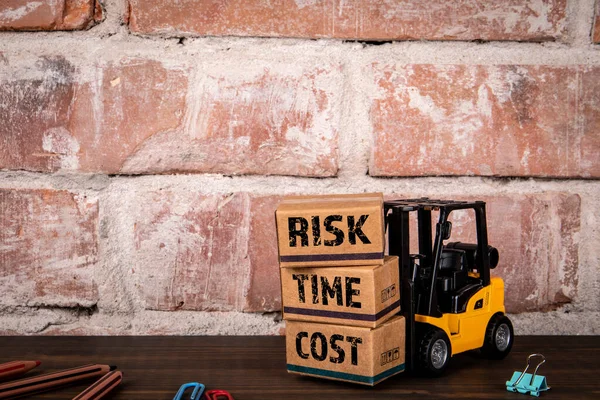 Risk, Time and Cost. Miniature cardboard boxes and a forklift on a wooden office table.