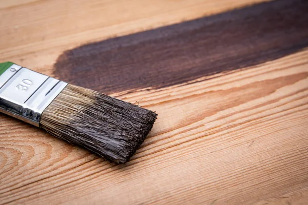 Brush with brown paint on a wooden texture background.