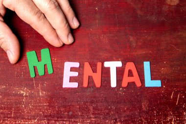 MENTAL. Ahşap arkaplanda renkli alfabe harflerinden metin.