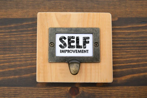 Self Improvement Concept. File cabinet label. Dark wooden background.