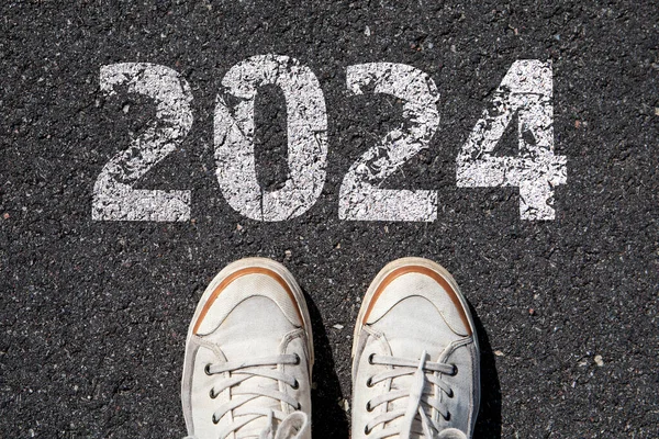 2024 Goals Concept. Human legs and shoes on asphalt background.