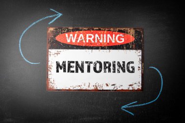 MENTORING kavramı. Kara karatahta arka planında metal uyarı işareti ve renkli tebeşir parçaları.