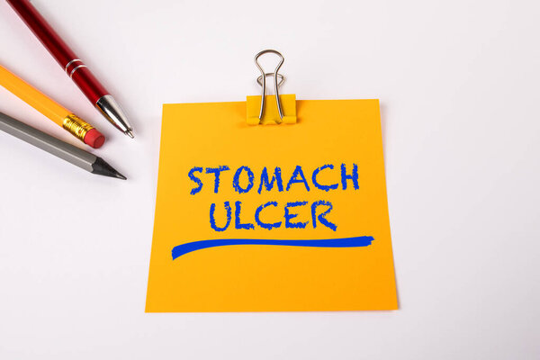 STOMACH ULCER. Yellow notepad and pen on white office table.