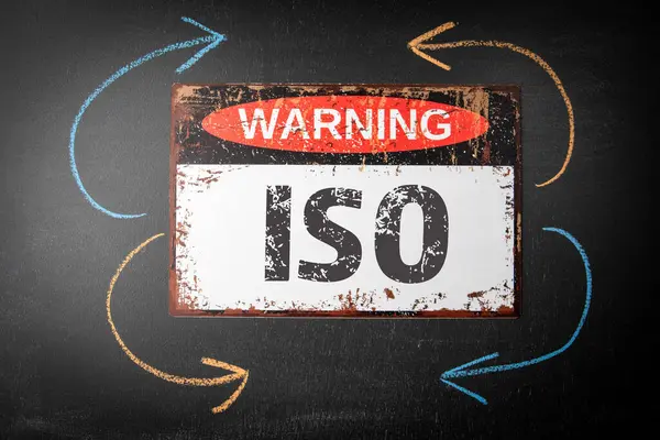ISO International Organization Standardization. Metal warning sign and colored pieces of chalk on a dark chalkboard background.