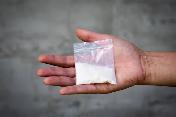 A bag of white powder in hand. Image for prohibited substances, addiction concept.