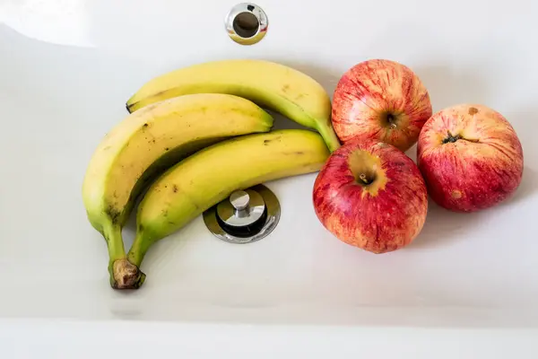Bananas and apples in a white sink. Fresh fruit.