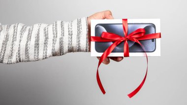Sigulda, Latvia - October 18, 2023: Box of the Iphone 15 Pro. Gift with a red ribbon in the hand on a white background clipart