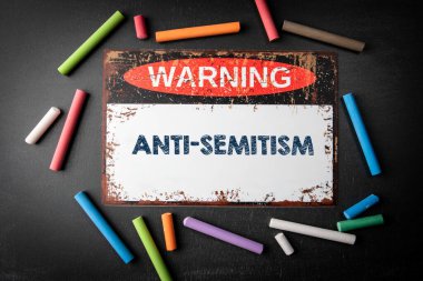 Anti-semitizm. Kara karatahta arka planında metal uyarı işareti ve renkli tebeşir parçaları.