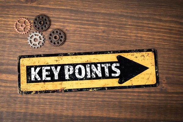 Key Points. Direction arrow and miniature gears on wood texture background.