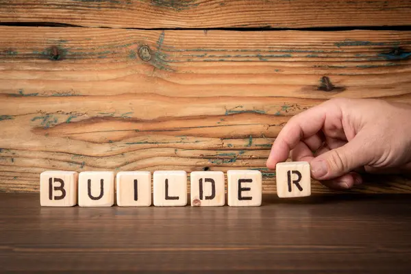 BUILDER. Alphabet blocks on wood texture background.
