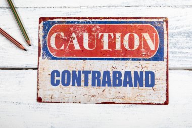 Kaçak mal. Metal CAOTION plaka beyaz ahşap arka plan üzerinde metin.