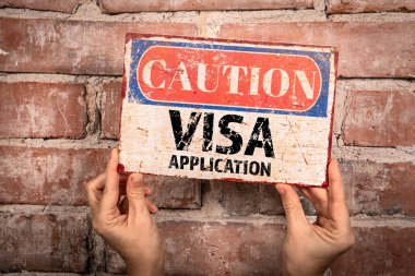 VISA Başvurusu. Bir kadının elinde tuğladan bir arka planda uyarı işareti.
