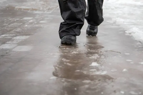 Ice on the sidewalk, close-up of walking with black boots on the slippery road.