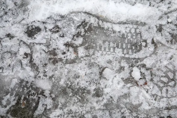 Frozen water on the sidewalk, footprints in the ice.