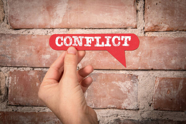 Conflict. Red speech bubble with text on a red brick background.