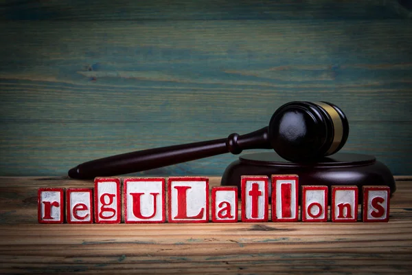 REGULATIONS. Red alphabet letters and judges gavel on wooden background. Laws and Justice concept.
