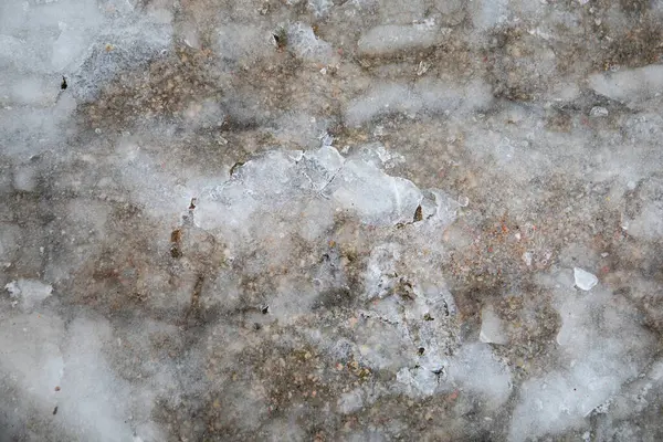 Ice covers the pavement on the sidewalk, close-up. Frozen puddle.