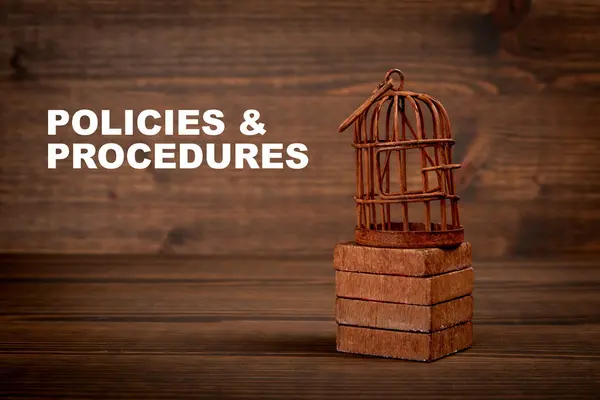 Policies and Procedures. Miniature birdcage on wood texture background.