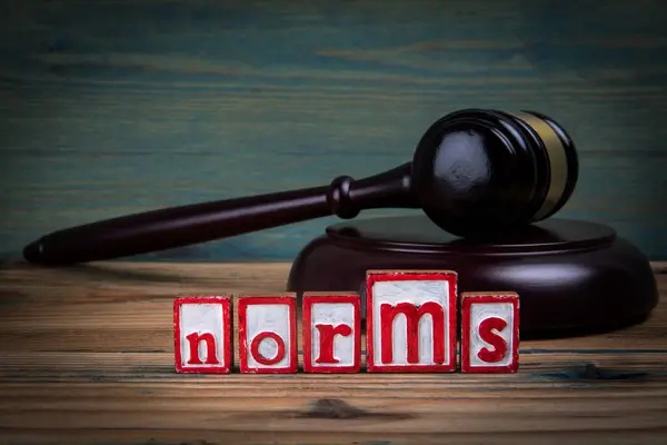 NORMS. Red alphabet letters and judges gavel on wooden background. Laws and justice concept.