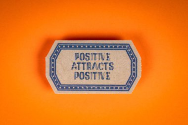 Pozitif Cazibe Pozitif. Turuncu arkaplanda yazı olan karton etiket.