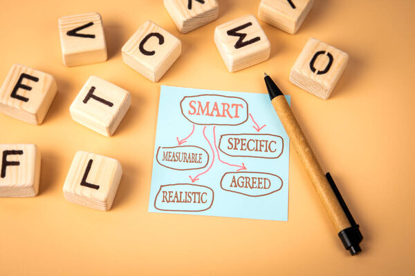 SMART. Конкретные измеряемые согласованные реалистичные. Блокнот и деревянные буквы алфавита на светлом фоне.