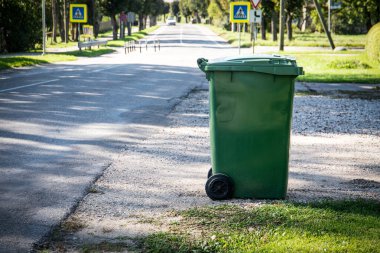 Caddenin kenarındaki yeşil çöp konteynırı. Kentsel çevre ve atık işleme endüstrisi.