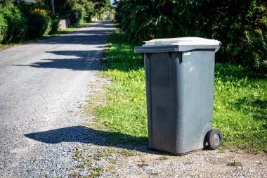 Caddenin kenarında gri bir çöp konteynırı var..